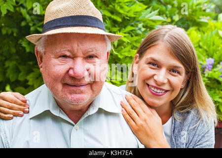 Lächelnd älterer Mann mit schönen jungen Enkelin im Park posing Stockfoto