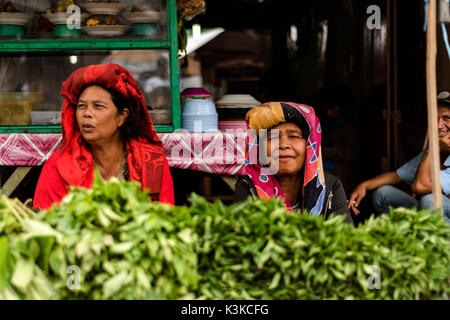 Zwei alte Frauen in ihrer pflanzlichen ausgeht, in der traditionellen Kleidung der Batak ethnische Gruppe. Im Hintergrund gibt es grinst ein Raucher. Auf dem Markt in Berastagi auf Sumatra, Indonesien. Stockfoto