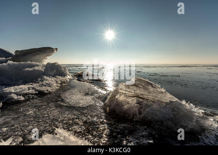 Die aufgehende Sonne ist auf dem Eis von der Bodden der deutschen Ostsee mit Rügen wider. Im Vordergrund gestapelt Eisschollen mit kleinen Eiskristalle. Stockfoto