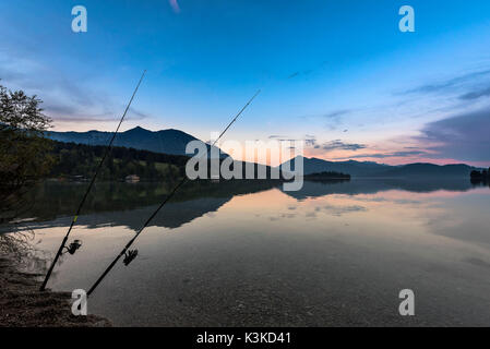 Zwei Angelruten in der Dämmerung in der kristallklaren Walchensee, im Hintergrund die Halbinsel Zwergern, Herzogstand und Jochberg. Stockfoto