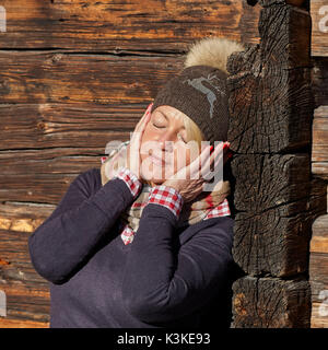 Blonde Frau mittleren Alters mit Kappe genießt die Sonne vor der Hütte, Porträt, Stockfoto