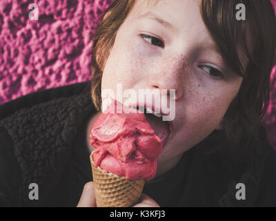 Porträt einer Youngster essen Erdbeer Eis vor einem rosa Hintergrund Stockfoto