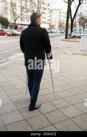 Ansicht von hinten von einem Mann auf der Straße mit Krücken Stockfoto