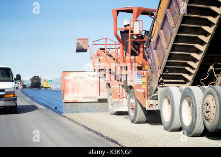 Eine orange Road resurfacing Maschine zur Festlegung von Kies auf einer einsamen Straße. Stockfoto