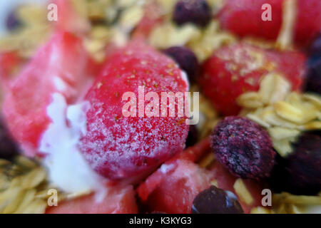 Eine Schale mit weißer Joghurt, geröstetes Müsli und gefrorene Erdbeeren und Blaubeeren. Stockfoto