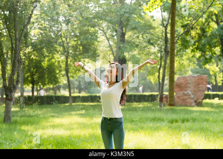 Happy stehendes Mädchen mit ihren Armen geöffnet, mit Blick auf die Sonne. Sonnenlicht schien in den Wald. Stockfoto