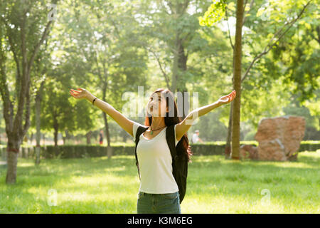 Happy stehendes Mädchen mit ihren Armen geöffnet, mit Blick auf die Sonne. Sonnenlicht schien in den Wald. Stockfoto