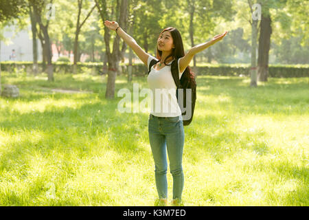 Happy stehendes Mädchen mit ihren Armen geöffnet, mit Blick auf die Sonne. Sonnenlicht schien in den Wald. Stockfoto