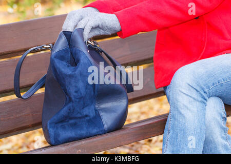 Frau sitzt auf der Bank im Herbst Park, öffnen ihre Handtasche und suchen verschiedene Dinge in Tasche Stockfoto