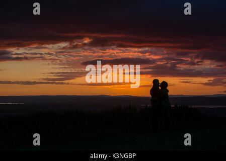 Ein paar Küssen, als Sie den Sonnenuntergang von Coaley Peak in Gloucestershire. Stockfoto