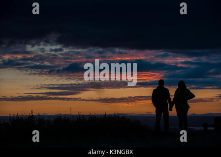 Ein paar halten Hände, da sie beobachten Sie den Sonnenuntergang von Coaley Peak in Gloucestershire. Stockfoto