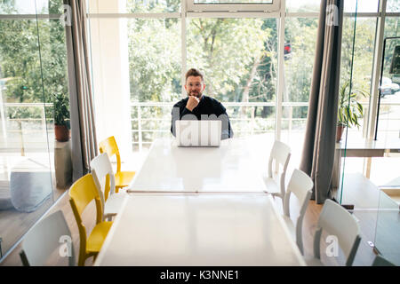 Hübscher junger Geschäftsmann mit Laptop allein in großen hellen Konferenzraum Stockfoto