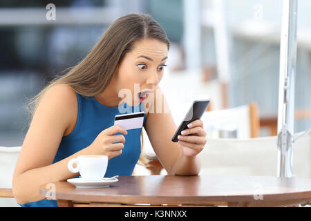 Single erstaunt Käufer holding Telefon und Kreditkarte, ein gutes Angebot auf der Linie in einem Restaurant sitzen Stockfoto