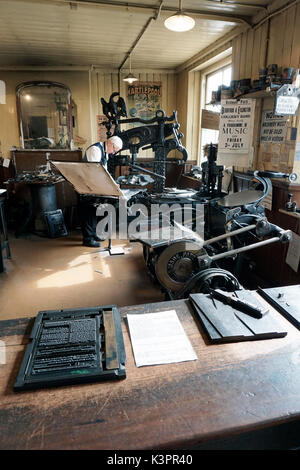 Ältere männliche Drucker arbeiten auf vintage Flachbett Buchdruck Maschine von Vintage Druckmaschinen umgeben Stockfoto