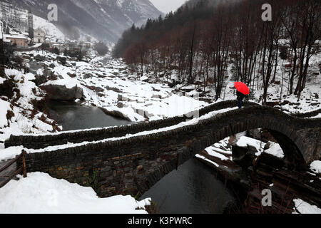 Das Mädchen mit dem roten Regenschirm auf Ponte dei Salti, Lavertezzo im Winter, Val Verzasca, Tessin, Schweiz Stockfoto