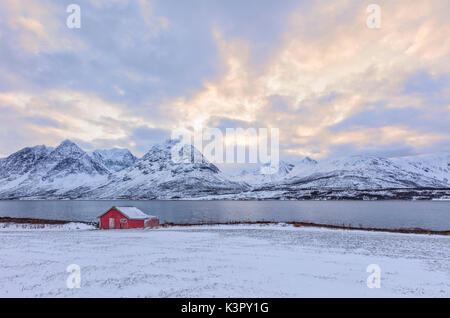 Typische Rorbu in der schneebedeckten Landschaft durch das gefrorene Meer und hohen Gipfeln Svensby Lyngen Alpen Tromsø Norwegen Europa umgeben Stockfoto