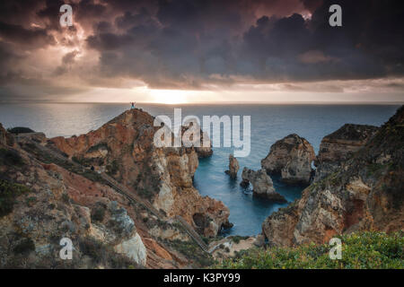 Wanderer auf Klippen am Meer unter dem bewölkten Himmel bei Sonnenaufgang Ponta da Piedade Lagos Algarve Portugal Europa umgeben Stockfoto