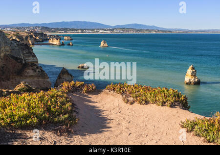 Ein sandiger Pfad in Richtung Praia Dona Ana Strand von türkisblauem Wasser des Ozeans und Klippen Lagos Algarve Portugal Europa umgeben Stockfoto