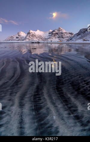 Wellen und Eis auf den surrealen Skagsanden Strand umgeben von schneebedeckten Gipfeln Flakstad Nordland county Lofoten Inseln Norwegen Europa Stockfoto