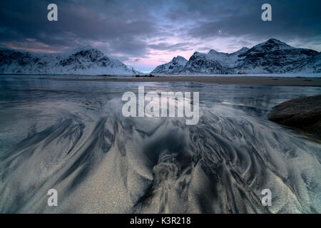 Wellen und Eis auf den surrealen Skagsanden Strand umgeben von schneebedeckten Gipfeln Flakstad Nordland county Lofoten Inseln Norwegen Europa Stockfoto