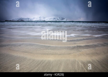 Wellen von der eisigen Meer am Strand im Hintergrund die schneebedeckten Gipfel Ramberg Lofoten Inseln Norwegen Europa Stockfoto