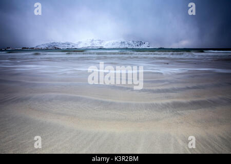 Wellen von der eisigen Meer am Strand im Hintergrund die schneebedeckten Gipfel Ramberg Lofoten Inseln Norwegen Europa Stockfoto