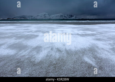 Wellen von der eisigen Meer am Strand im Hintergrund die schneebedeckten Gipfel Ramberg Lofoten Inseln Norwegen Europa Stockfoto