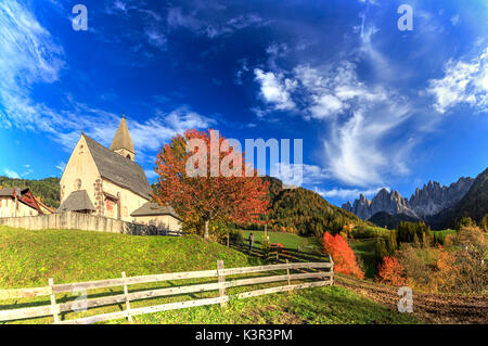 Panorama der Kirche St. Magdalena in den Farben des Herbstes eingetaucht. Im Hintergrund die Geisler Berge. Val di Funes. Stockfoto