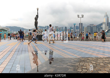 Touristen zu Fuß in der Nähe der Bronze Statue von Hong Kong Film Awards und Skyline in Avenue der Stars, China Stockfoto