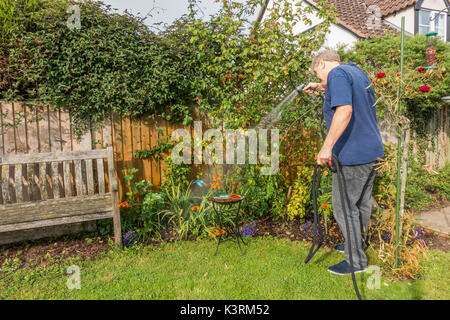 Ein älterer Mann Bewässerung seinen Garten Pflanzen, Anfang Herbst, mit Schlauch und Sprühvorrichtung. Langtoft, Lincolnshire, England, UK. Stockfoto