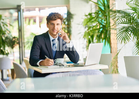 Portrait von stattlicher Junge Unternehmer sprechen per Telefon und lächelnd während der Arbeit im Café während der Kaffeepause Stockfoto