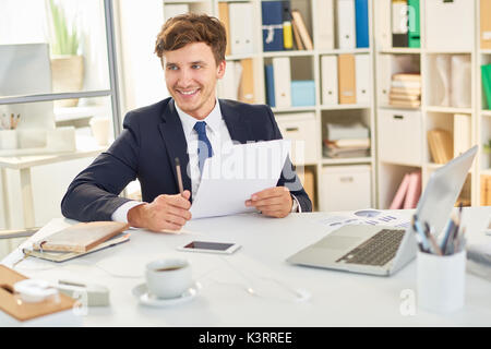 Portrait von lächelnden jungen Geschäftsmann am Schreibtisch im Büro, Lesen der Dokumentation Stockfoto