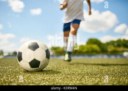 Niedrige Abschnitt Portrait von unkenntlich Teenager treten Kugel während der Fußball-Praxis, Schwerpunkt auf der Kugel liegen auf Gras Stockfoto