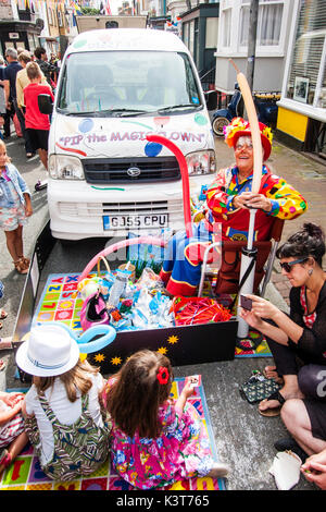 English Town Street Fair. Reife Frauen gekleidet, wie PIP die Magie clown, Ballontiere für Kinder. Das Sitzen auf Stuhl in der Straße mit ihren Business van Neben ihr geparkt. Stockfoto