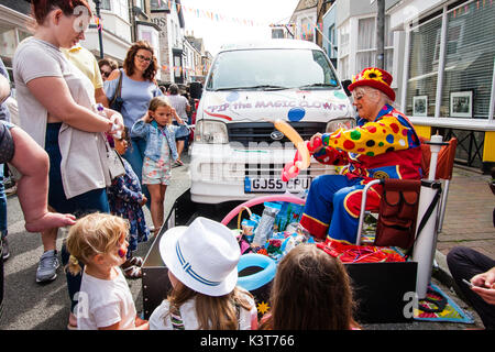 English Town Street Fair. Reife Frauen gekleidet, wie PIP die Magie clown, Ballontiere für Kinder. Das Sitzen auf Stuhl in der Straße mit ihren Business van Neben ihr geparkt. Stockfoto