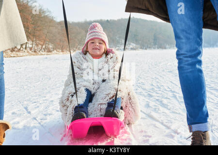 Kind Rodeln oder Rodeln auf Schnee mit Ihren glücklichen Familie Stockfoto