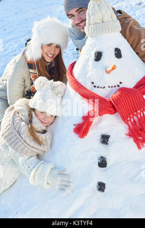 Kind baut Schneemann mit ihrer Familie im Winter und Spielen Stockfoto