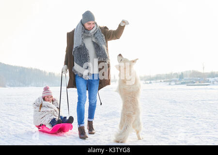 Vater spielen mit Hund und Tochter, während Rodelbahn im Winter Stockfoto