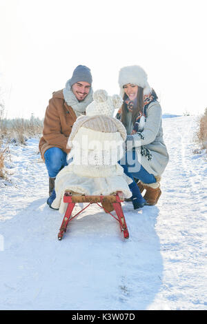 Glückliche Eltern spielen mit Kind auf Schlitten im Winter im Schnee Stockfoto