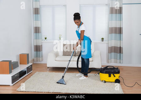 Junge afrikanische Frau Reinigung Teppich mit Staubsauger Stockfoto