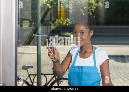 Afrikanische Frau reinigen Glas mit Gummi Glasreiniger von Außerhalb Stockfoto