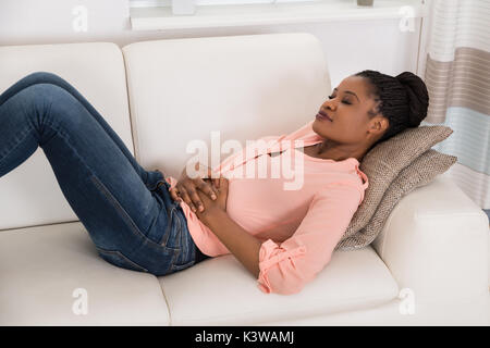 Junge afrikanische Frau liegt auf einem Sofa Leiden von Magenschmerzen Stockfoto