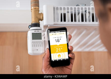 Nahaufnahme von einer Person Hand Einstellen der Temperatur am Thermostat mit Handy Stockfoto