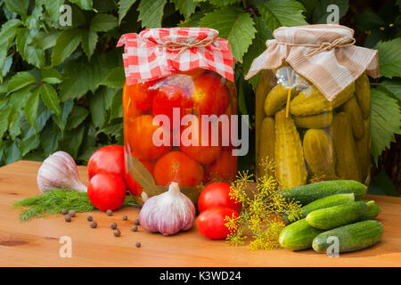 Konserven und frischem Gemüse. Dosentomaten und eingelegte Gurken in Gläsern auf hölzernen Tisch outdoor. hausgemachte Konserven Gemüse. Stockfoto