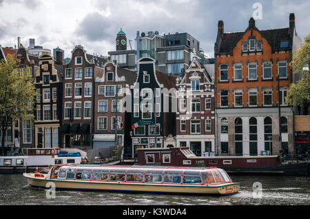Amsterdam, Niederlande - 27 April 2017: Cruise touristische Boot gegen Hausboote, Bargen und typische Kurven niederländischen Häusern mit großen Fenstern in B Stockfoto