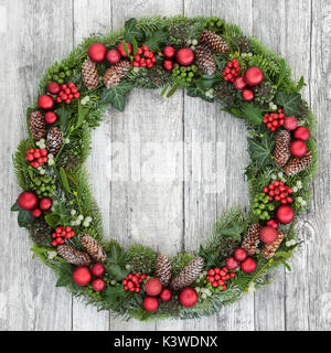 Christmas wreath Dekoration mit roten Kugeln, Holly, Mistel, Tannenzapfen, Juniper, Tanne, Fichte, Zeder, und Efeu auf Distressed weißem Holz Vorderseite tun Stockfoto