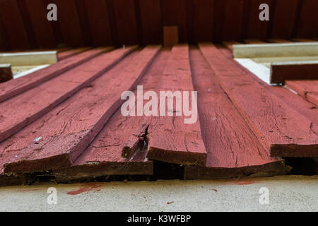 Ein Rot lackiertes Holz Fassade an einem Haus, das in der unteren ersetzt Reparatur verdorben ist. Stockfoto