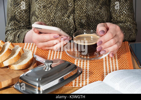 Glas Becher mit schwarzem Kaffee und Telefon in weibliche Hände mit Maniküre Stockfoto