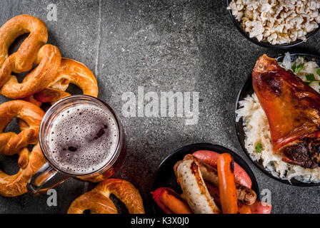 Auswahl der traditionelle deutsche Küche Oktoberfest. Bier, gebackenem Schweinefleisch Schaft, Popcorn, eine Auswahl an verschiedenen Würste, hausgemachte Brezeln. Auf einem schwarzen Sto Stockfoto