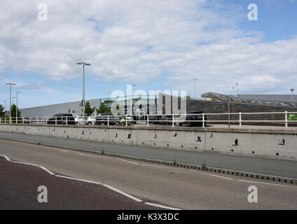 Blick auf das Wassersportcenter Port Eirias von der Hauptstraße aus, ohne Verkehr und mit Gehweg, Betonmauer und weißer Schutzgeländer in Nord-wales, großbritannien Stockfoto